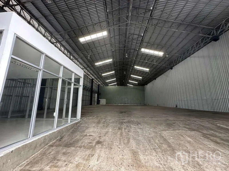 货栈 出租在Pak Kret, Nonthaburi - 高挑仓库大厅，照明充足，混凝土地面，侧边有办公室。