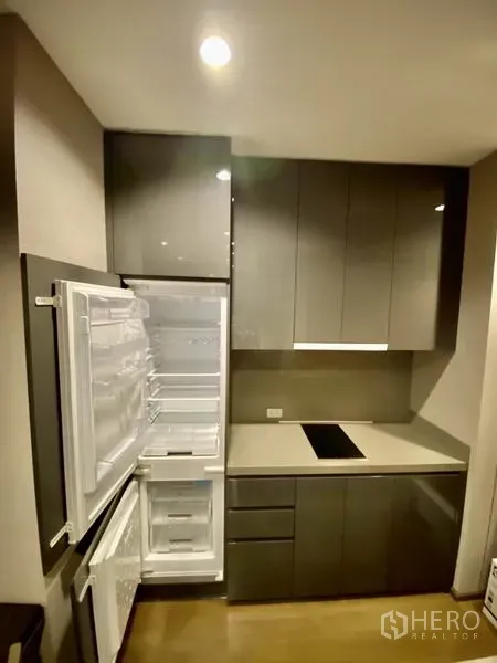 Condominium for rent or sale in Bang Rak, Bangkok - Close-up of sleek kitchen with integrated refrigerator open, induction hob and ample storage.