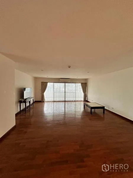 Condominium for rent in Bangkok - Spacious lounge with wood floors, TV stand, coffee table and sheer-curtained windows.