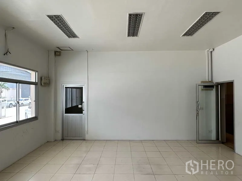 Factory for rent in Samut Prakan - Ground-floor office room with large window, tiled floor and access door to the yard.