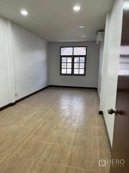 Townhouse for rent in Din Daeng, Bangkok - Long bedroom with wood-look flooring, recessed ceiling lights, and a window for natural light.