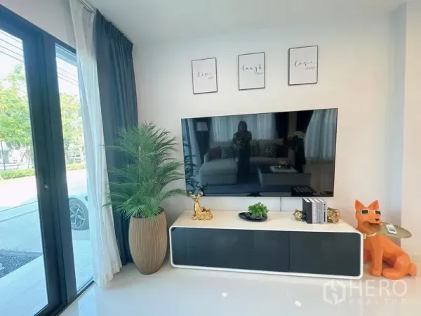 Detached House for rent or sale in Bang Phli, Samut Prakan - Contemporary living corner with large TV on a wall-mounted console, floor-to-ceiling curtains and decor.