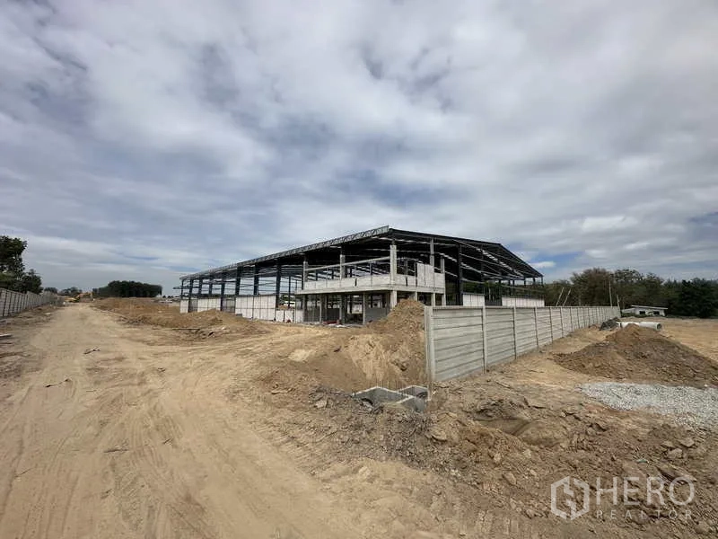 货栈 出租或出售在Nikhom Phatthana, Rayong - 仓库外角观，建筑外壳与围栏及现场通道一览。