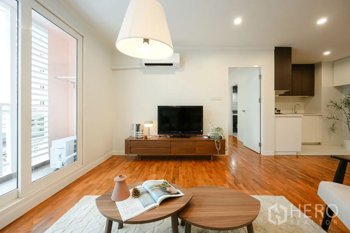 公寓 for sale in Watthana, Bangkok - 客厅朝向木质电视柜，旁有阳台门与邻接小厨房。