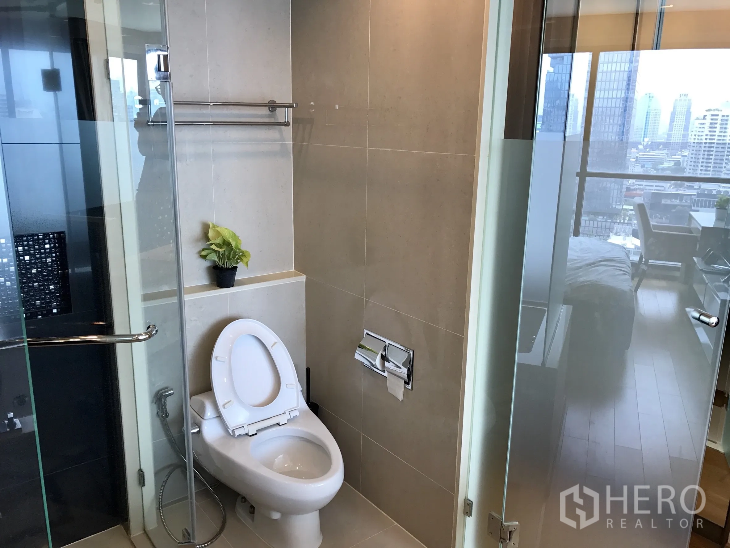 Condominium for rent or sale in Bang Rak, Bangkok - Bright bathroom with glass shower and toilet, city view through door.