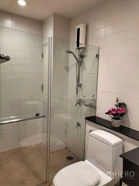 Condominium for rent in Watthana, Bangkok - Bathroom with white tiles, glass-enclosed shower, toilet and countertop shelf.