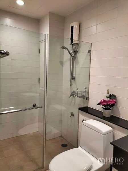 Condominium for rent in Watthana, Bangkok - Bathroom with white tiles, glass-enclosed shower, toilet and countertop shelf.