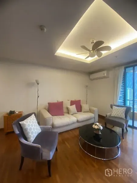 Condominium for rent in Pathum Wan, Bangkok - Living area with sofa and armchairs around a black round table under recessed ceiling lights and balcony access.