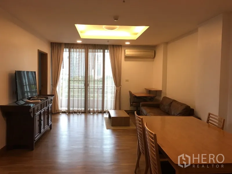 คอนโด ให้เช่าในPathum Wan, Bangkok - ห้องนั่งเล่นสว่างพื้นไม้ ฝ้าหลุม ตู้วางทีวี โซฟา ชุดโต๊ะทานข้าว และประตูกระจกเต็มบานเปิดสู่ระเบียงวิวเมือง