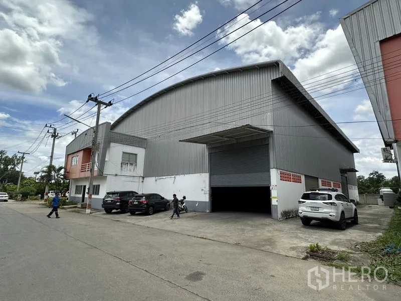 工厂 出租在Phra Nakhon Si Ayutthaya - 街景视角的大型钢板外墙工厂，弧形屋顶，宽阔卷闸门与前方停车位。