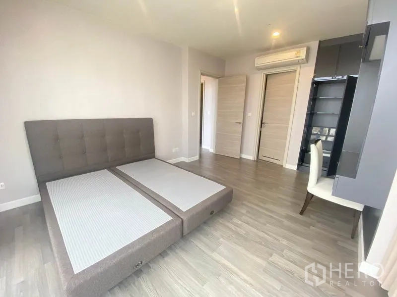 Condominium for rent in Bang Rak, Bangkok - Spacious bedroom with upholstered bedframe, desk and air-conditioning unit.