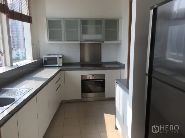 Condominium for rent in Khlong Toei, Bangkok - Modern closed kitchen featuring granite countertops, white cabinetry, built-in oven, microwave, and a large window.