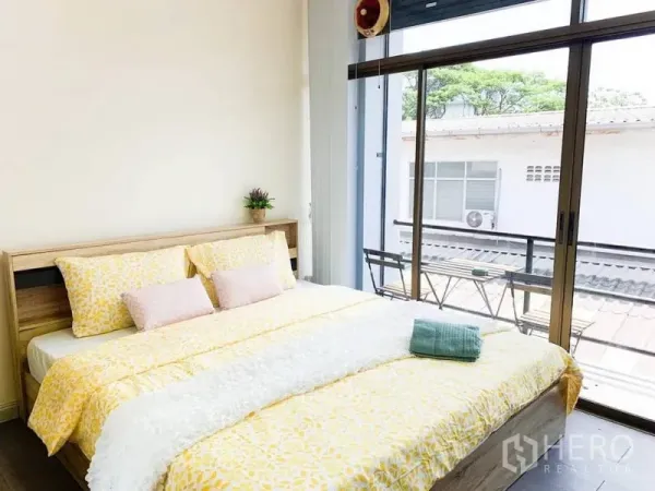 Home Office for rent in Khlong Toei, Bangkok - Sunlit bedroom with king bed and sliding glass doors to a small balcony with table set.