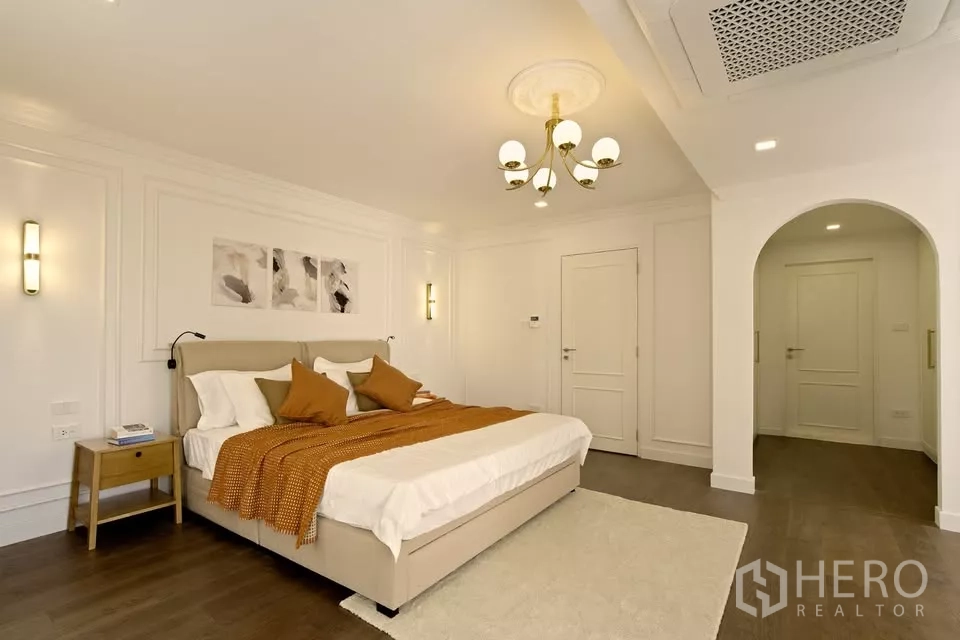 Condominium for sale in Watthana, Bangkok - Primary bedroom in Bangkok condo with chandelier, wall molding and warm accent bedding.
