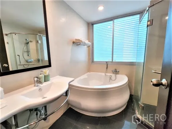 Condominium for rent in Bang Rak, Bangkok - Bright bathroom featuring a round soaking tub, glass shower enclosure, wall-mounted sink and frosted window.
