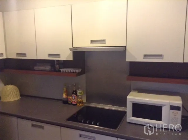 Condominium for rent or sale in Din Daeng, Bangkok - Fitted kitchen with white cabinets, electric cooktop, hood, ample countertop space, and a microwave.