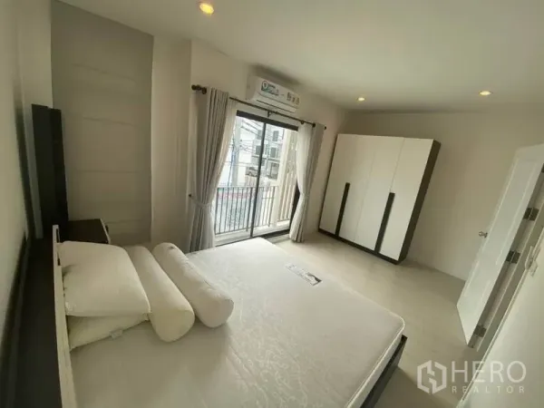 Townhouse for rent or sale in Bang Kapi, Bangkok - Bright master bedroom with sliding glass doors to a balcony, air conditioning and a large wardrobe.