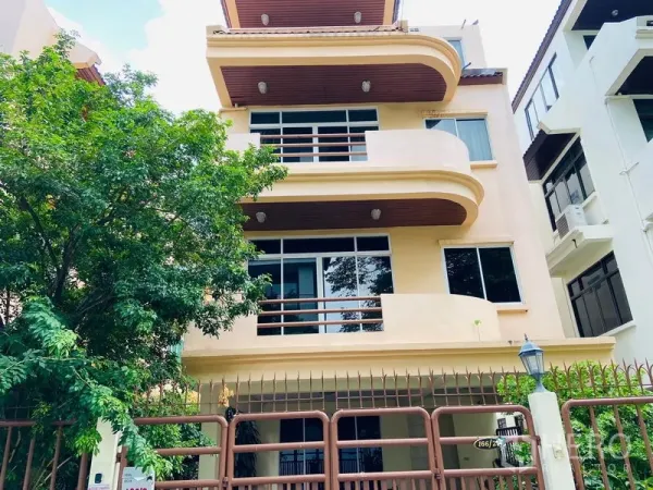 Detached House for rent in Watthana, Bangkok - Three-storey beige detached house with curved balconies, large windows and a gated frontage.