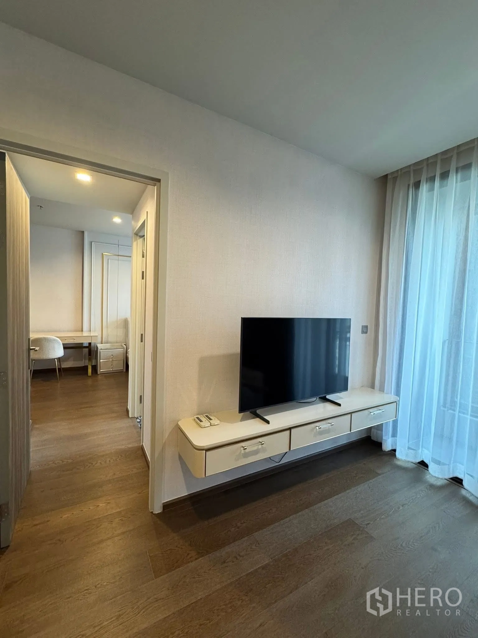 Condominium for rent in Khlong Toei, Bangkok - Living wall with floating TV console and sheer drapes.