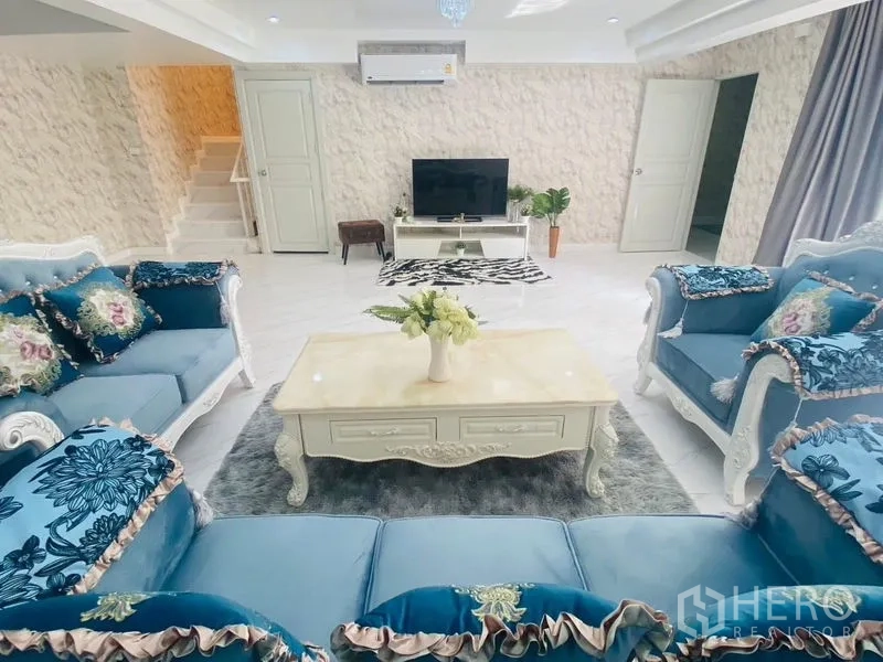 Condominium for rent or sale in Watthana, Bangkok - Living room with TV console, ornate coffee table and matching blue sofas.