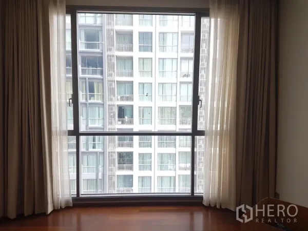公寓 出售在Watthana, Bangkok - 落地窗配薄纱窗帘与木地板，可眺望对面公寓外立面。