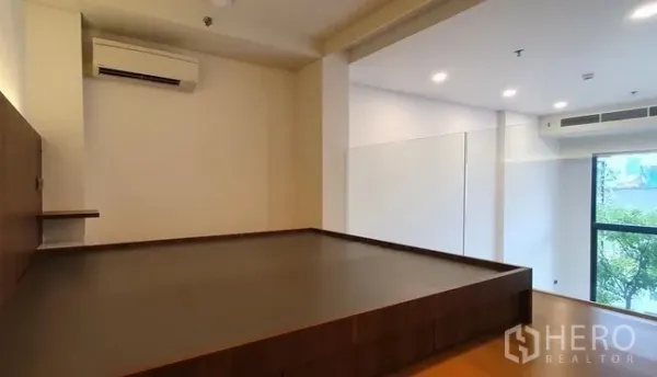 Condominium for sale in Watthana, Bangkok - Spacious loft bedroom platform with air conditioning and a large window overlooking greenery.