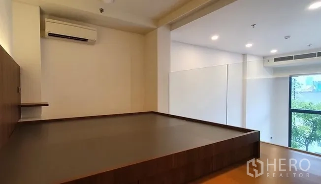 Condominium for sale in Watthana, Bangkok - Spacious loft bedroom platform with air conditioning and a large window overlooking greenery.