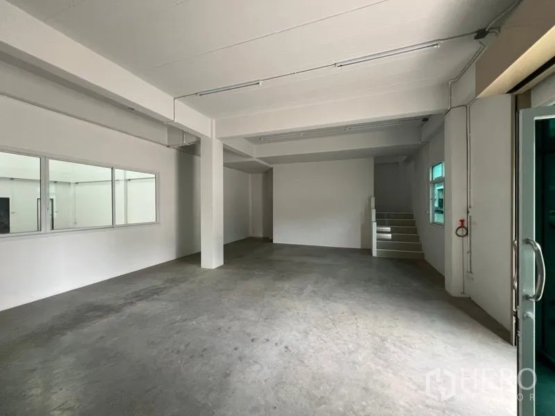 Factory for rent in Phra Samut Chedi, Samut Prakan - Open-plan ground level area with large windows, stair access and ample lighting.