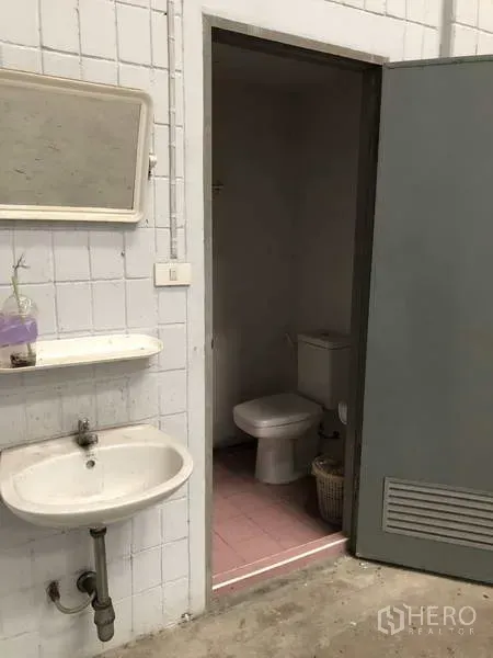 货栈 出租在Lat Lum Kaeo, Pathum Thani - 工业风卫生间入口，墙挂式洗手盆与镜子，旁有马桶间。