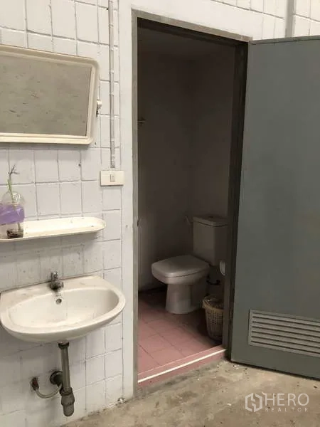 货栈 出租在Lat Lum Kaeo, Pathum Thani - 工业风卫生间入口，墙挂式洗手盆与镜子，旁有马桶间。