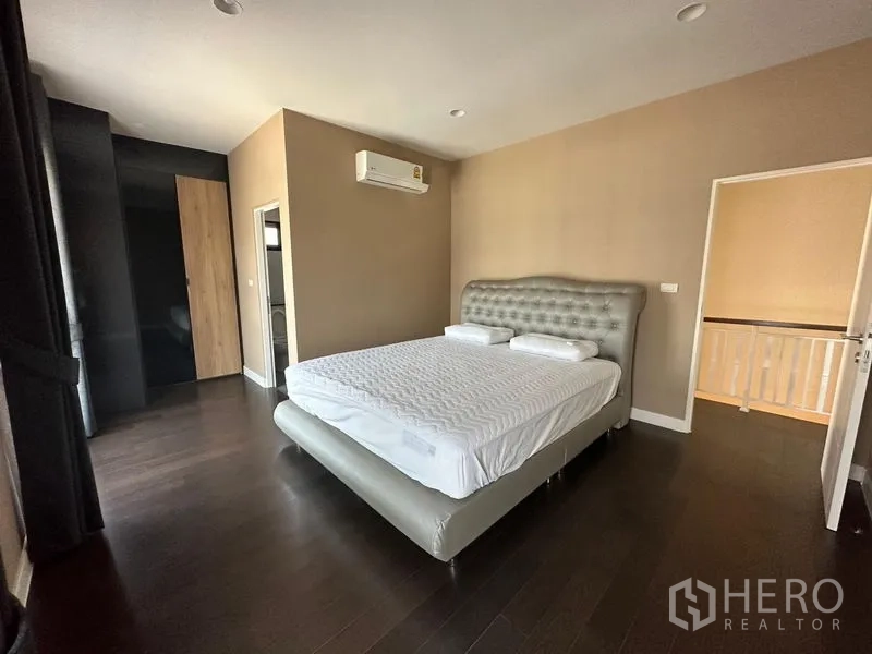Detached House for rent or sale in Lam Luk Ka, Pathum Thani - Second bedroom with upholstered bed, air conditioner, dark wood floor and wardrobe.