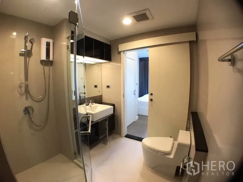 Condominium for rent in Khlong Toei, Bangkok - Bright bathroom with glass-enclosed shower, vanity and toilet.