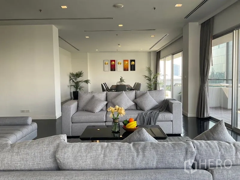 Apartment for rent in Sathon, Bangkok - Spacious lounge with grey sofas facing the dining area and terrace.