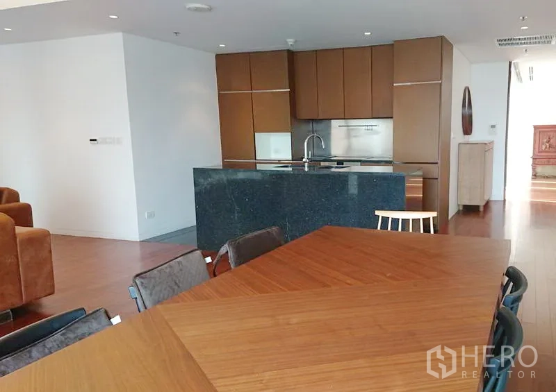 Condominium for sale in Pathum Wan, Bangkok - Modern kitchen with dark stone island, wood cabinetry, built-in appliances and adjacent dining table.