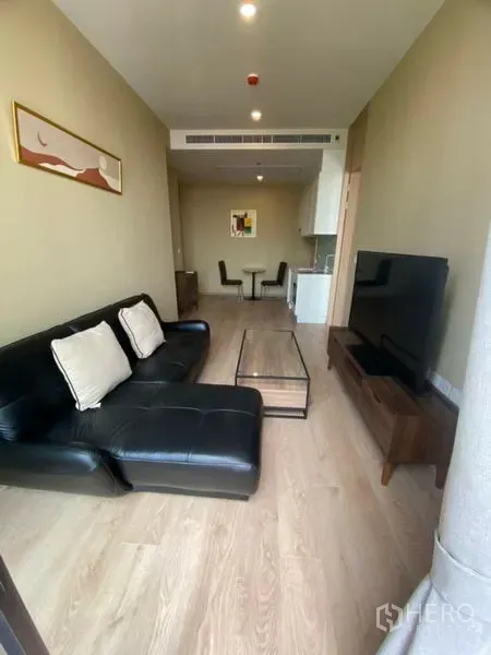 公寓 出租在Watthana, Bangkok - 开放式客厅，黑色皮沙发、电视柜与浅色木地板。