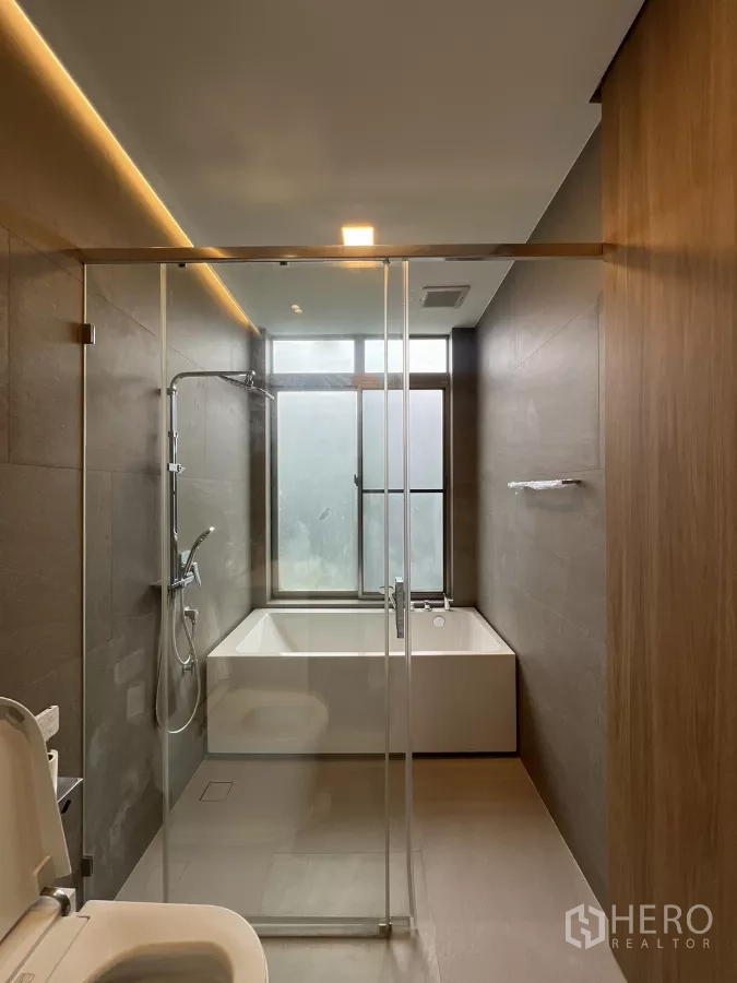 Detached House for rent in Saphan Sung, Bangkok - Bathroom with glass shower and bathtub by a frosted window.