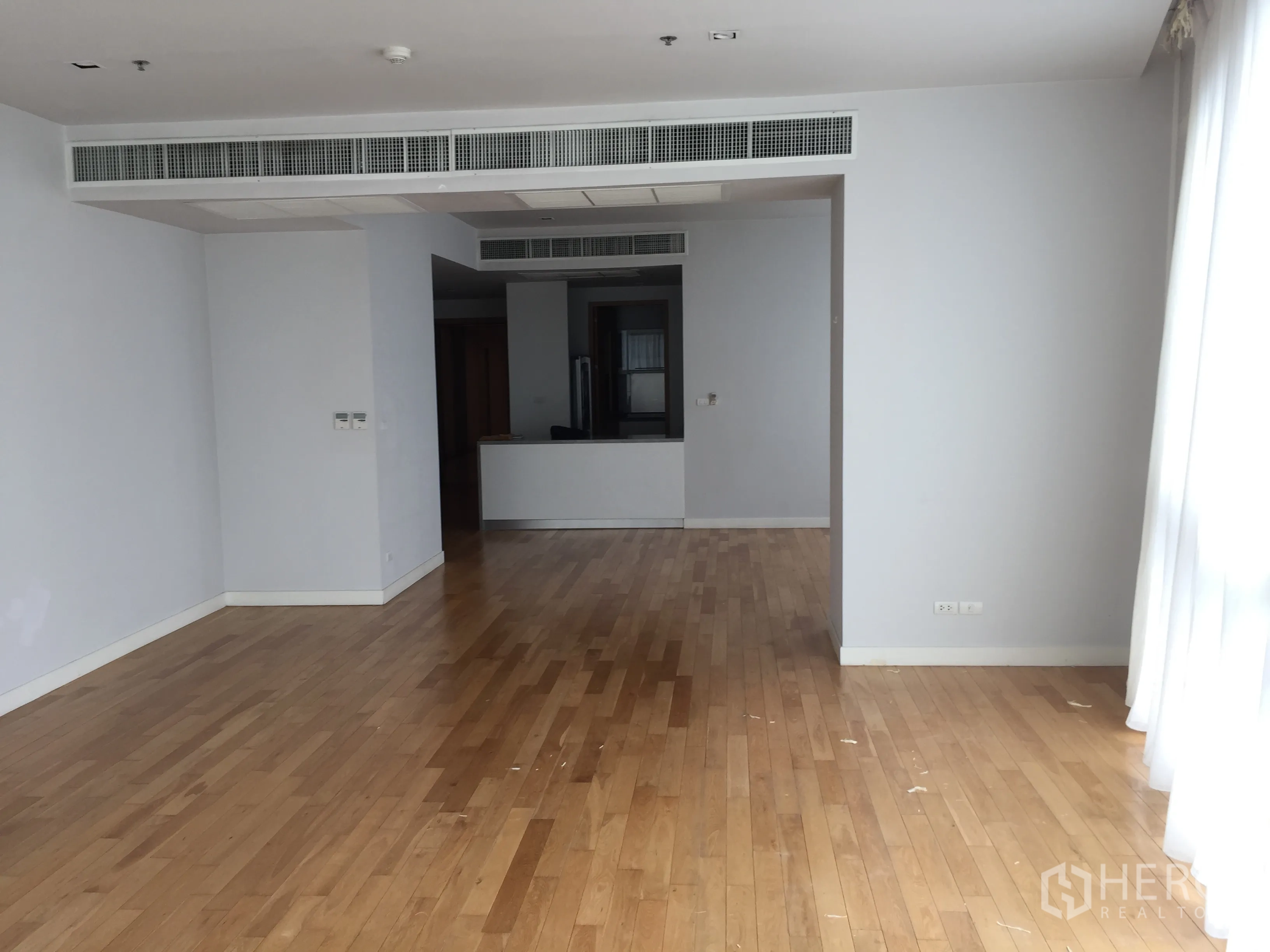 Condominium for rent in Khlong Toei, Bangkok - Open-plan living and dining area with light wood floors, ducted air-conditioning and full-height windows.