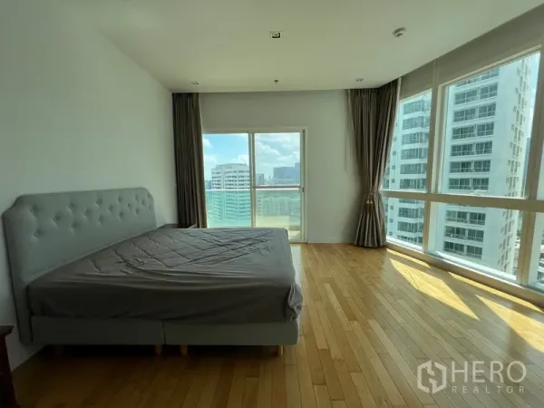 Condominium for rent in Khlong Toei, Bangkok - Master bedroom with wraparound windows, balcony door and warm wood floors.