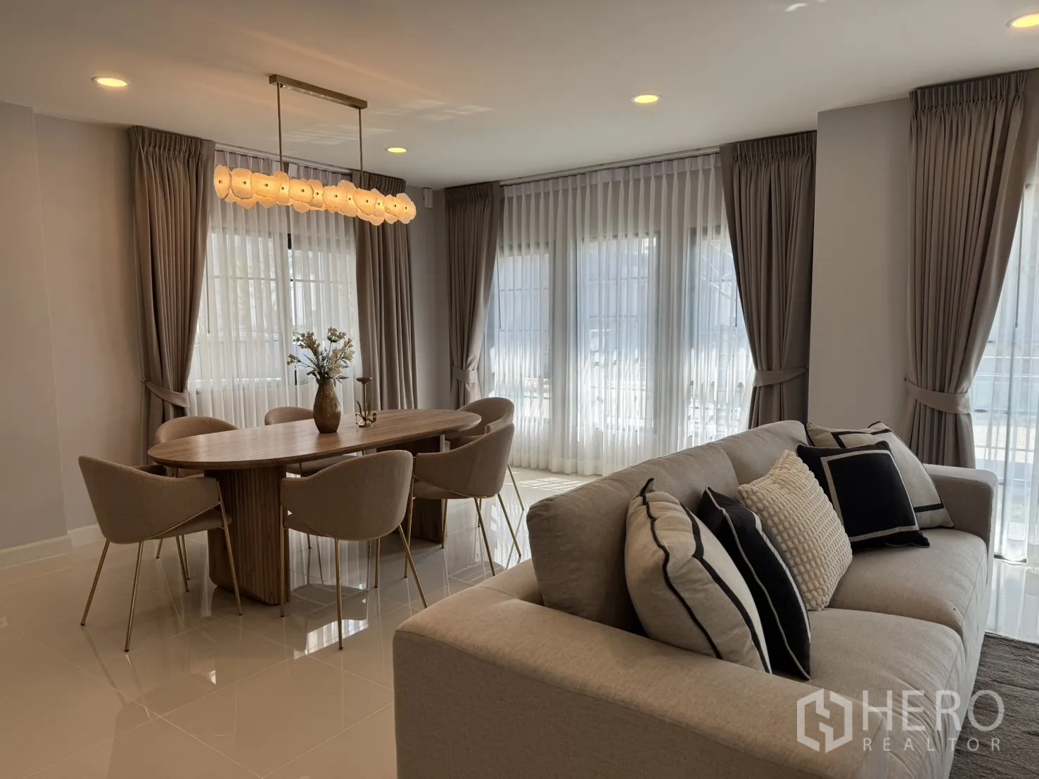 บ้าน for rent in Bang Phli, Samut Prakan - โถงนั่งเล่นและรับประทานอาหารแบบเปิดโล่ง โซฟาสีเบจ โต๊ะไม้ทรงวงรี โคมแขวน และหน้าต่างบานใหญ่