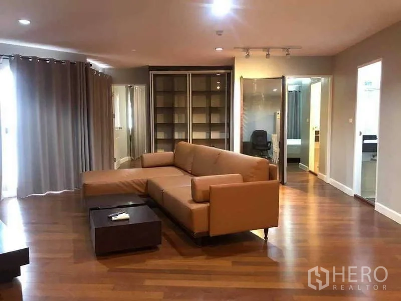 Condominium for sale in Yan Nawa, Bangkok - Spacious living room with L-shaped leather sofa, shelving and wood floors.