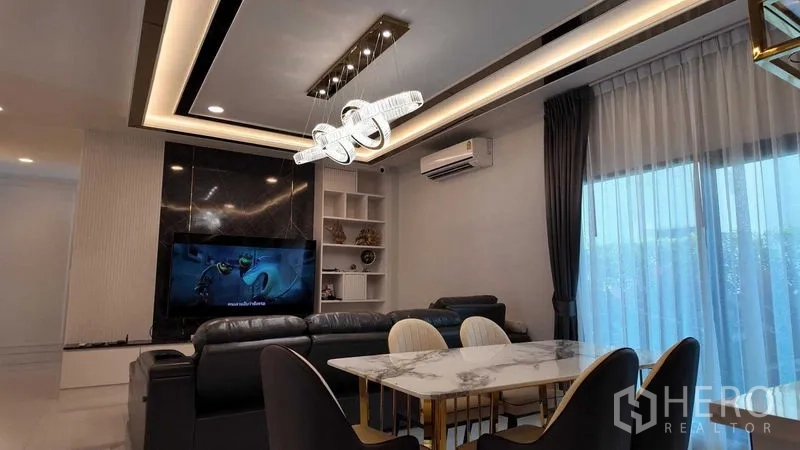 บ้าน ให้เช่าหรือขายในBang Na, Bangkok - ห้องนั่งเล่นพร้อมโซฟาชุด ผนังทีวี และไฟเพดานดีไซน์ เชื่อมต่อโซนทานอาหาร