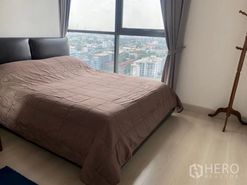Condominium for sale in Phra Khanong, Bangkok - Bedroom with large window, city view and double bed with gray curtains
