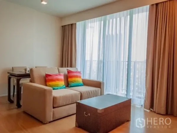 公寓 出租在Watthana, Bangkok - 明亮客厅，沙发与彩色抱枕、茶几、餐桌，落地窗通向阳台。