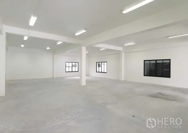 Warehouse for rent in Samut Prakan - Spacious white warehouse floor with columns, windows and bright strip lighting ready for storage or production.