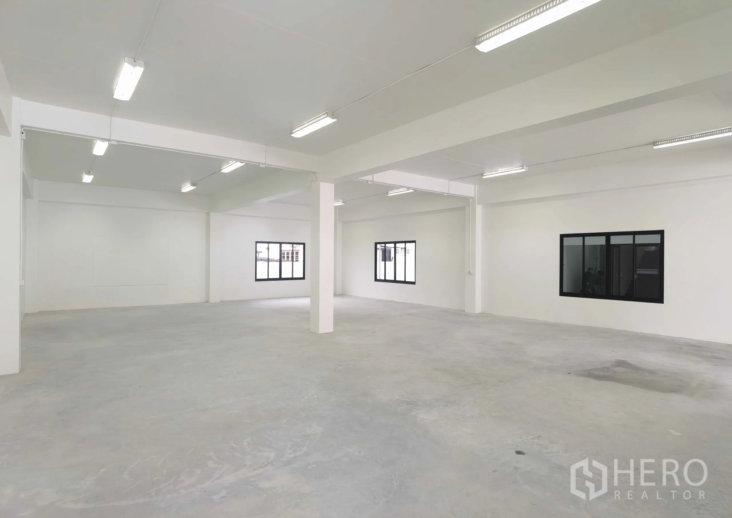 Warehouse for rent in Samut Prakan - Spacious white warehouse floor with columns, windows and bright strip lighting ready for storage or production.