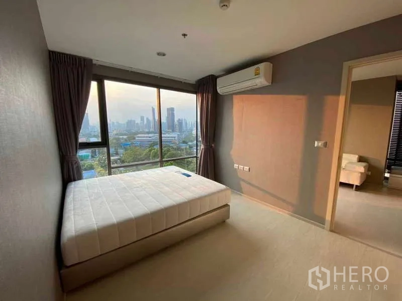 Condominium for rent or sale in Khlong Toei, Bangkok - Corner bedroom with queen bed, wall A/C and panoramic city view through wide glazing.