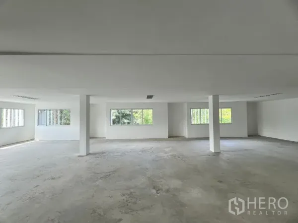 零售空间 出租在Huai Khwang, Bangkok - 明亮的开放式零售楼层，白色墙面与混凝土地面，立柱与大窗户可见绿景。
