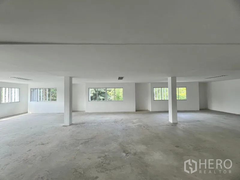零售空间 出租在Huai Khwang, Bangkok - 明亮的开放式零售楼层，白色墙面与混凝土地面，立柱与大窗户可见绿景。