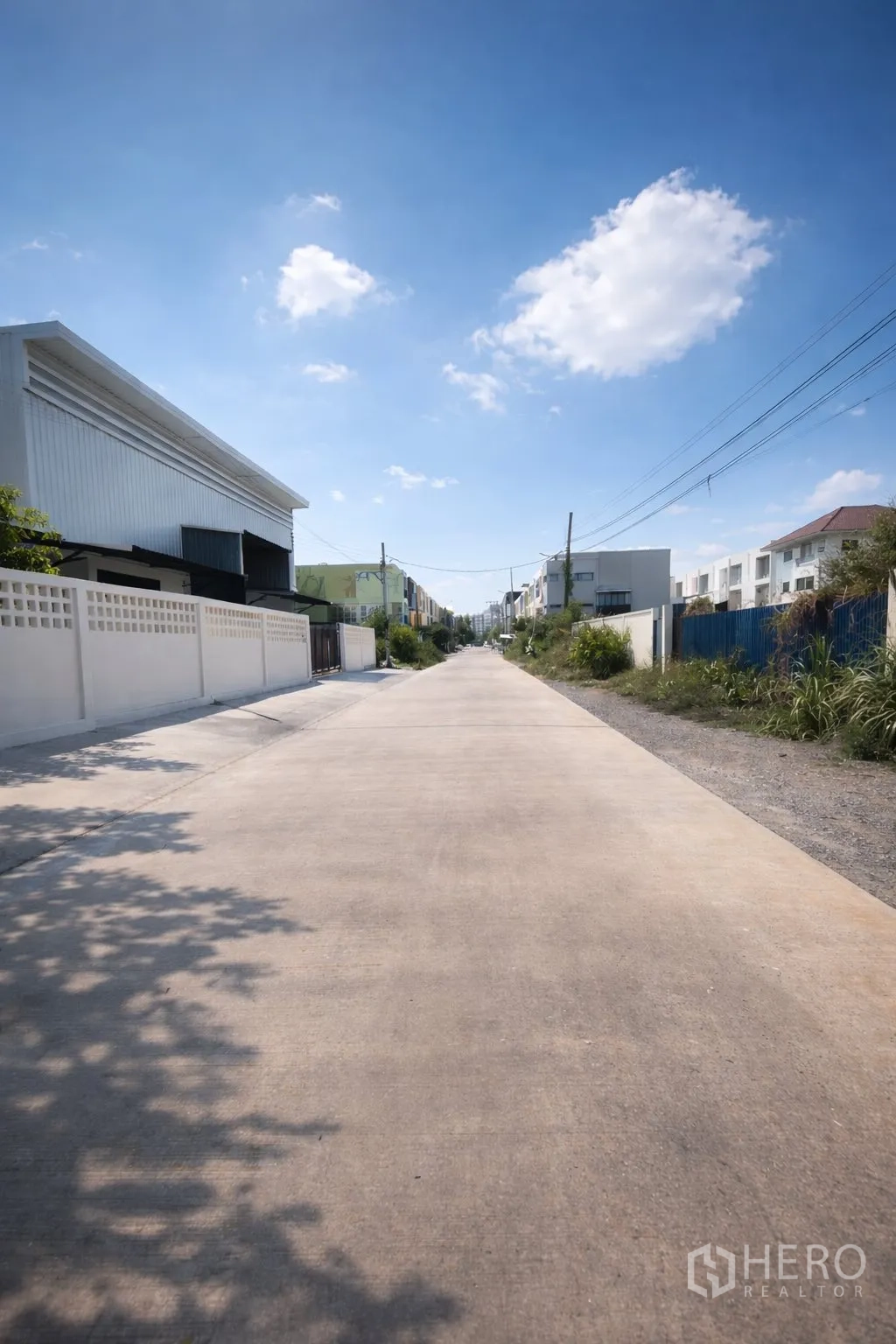 Warehouse for rent in Prawet, Bangkok - Wide concrete access road in front of low-rise warehouses and homes.