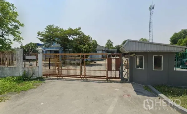 Warehouse for rent in Sam Phran, Nakhon Pathom - Gated warehouse entrance with guardhouse and wide concrete driveway.